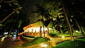 A well-lit resort with a covered outdoor area, palm trees, and a stone pathway. - Four Oceans Resort Muine (Mui Ne)