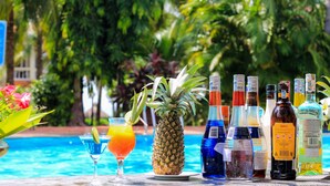 A poolside table with a pineapple, a cocktail, and various bottles of alcohol. - Four Oceans Resort Muine (Mui Ne)