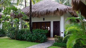A thatched-roof bungalow with a stone pathway leading to the entrance, surrounded by lush tropical vegetation. - Cham Villas (Mui Ne)
