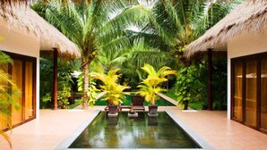 A pool area with lounge chairs and palm trees. - Cham Villas (Mui Ne)