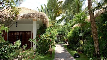 Un sendero en un jardín tropical que lleva a una edificación de techo de paja y puerta de madera.