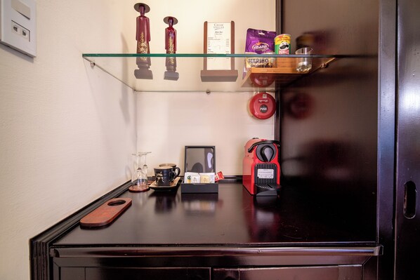 A compact kitchenette with a refrigerator, a coffee machine, a wine glass, and a small shelf with snacks. - Cham Villas (Mui Ne)
