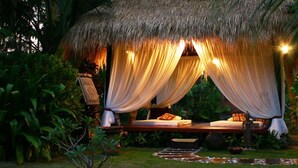 A thatched-roof outdoor bedroom with a bed, draped curtains, and ambient lighting. - Cham Villas (Mui Ne)