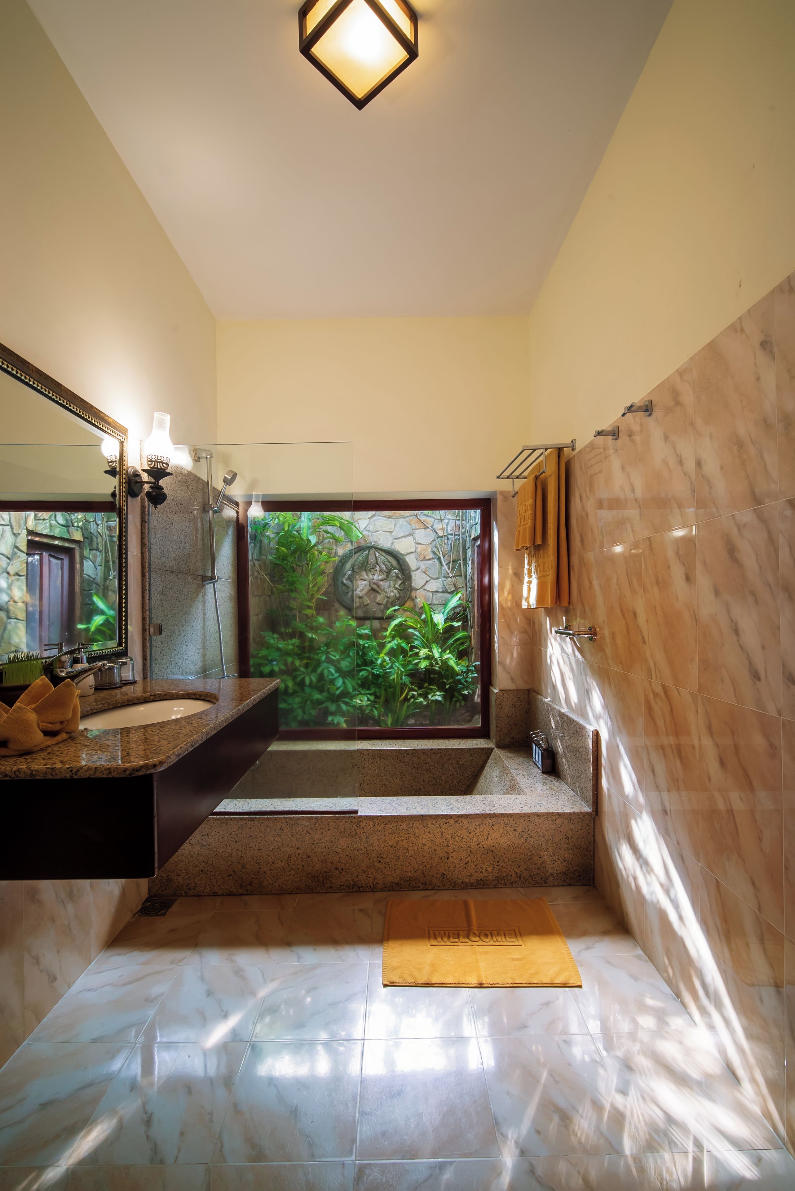 Un baño con un espejo grande, un lavabo, una bañera y vistas a un jardín verde a través de una puerta de cristal.