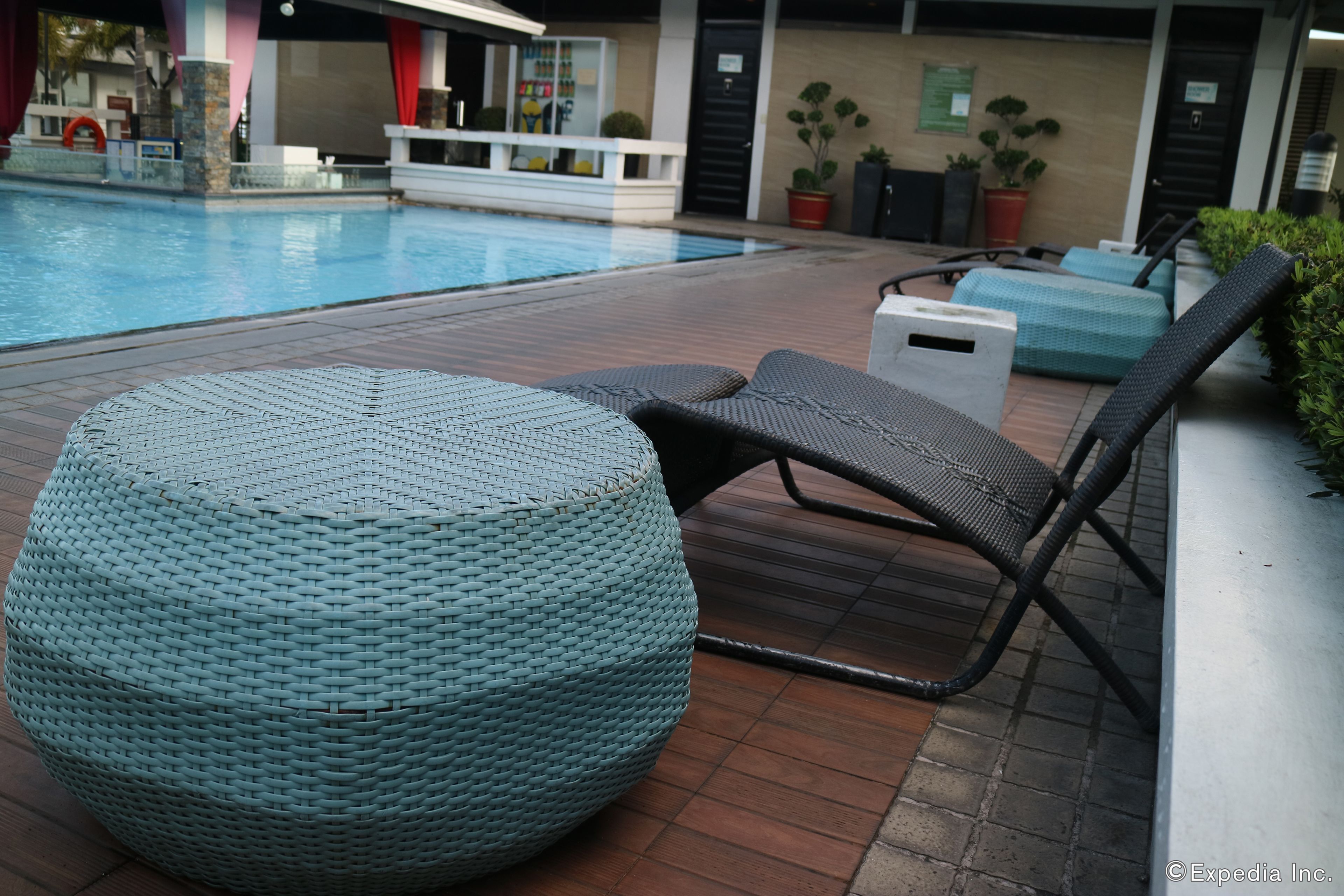 Zona junto a la piscina con un otoman tejido redondo, una silla de descanso negra y una pequeña mesa.
