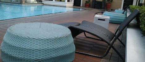A poolside area with a round woven ottoman, a black lounge chair, and a small table.