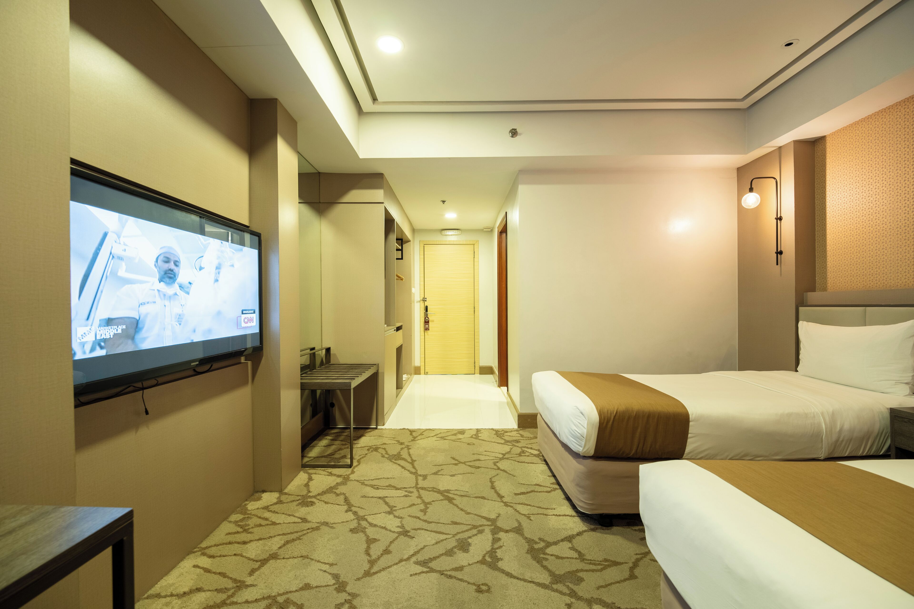 A hotel room with a television, two beds, a desk, and a carpeted floor.