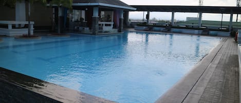A swimming pool with a covered area and a building in the background.