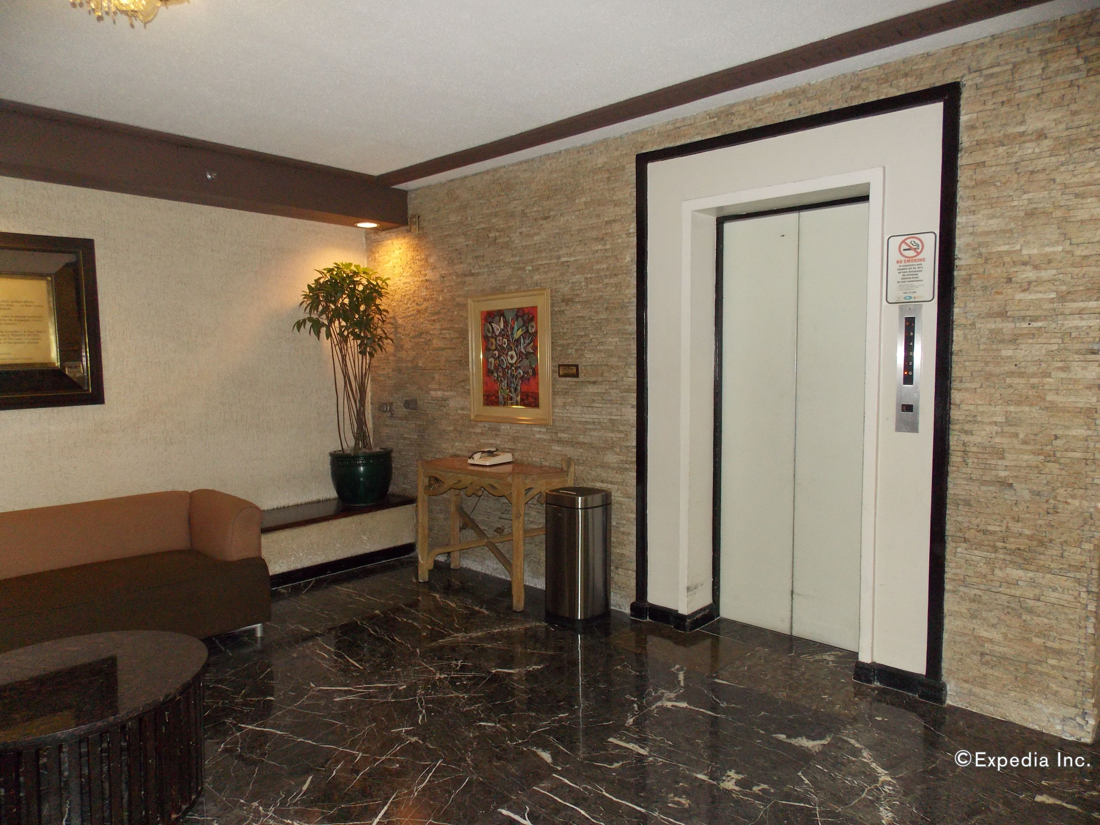 A lobby with a marble floor, a reception desk, a potted plant, a painting, and an elevator.