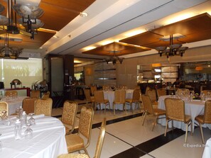 A restaurant with multiple tables and chairs, a kitchen area visible through the glass wall, and a projection screen displaying an image.