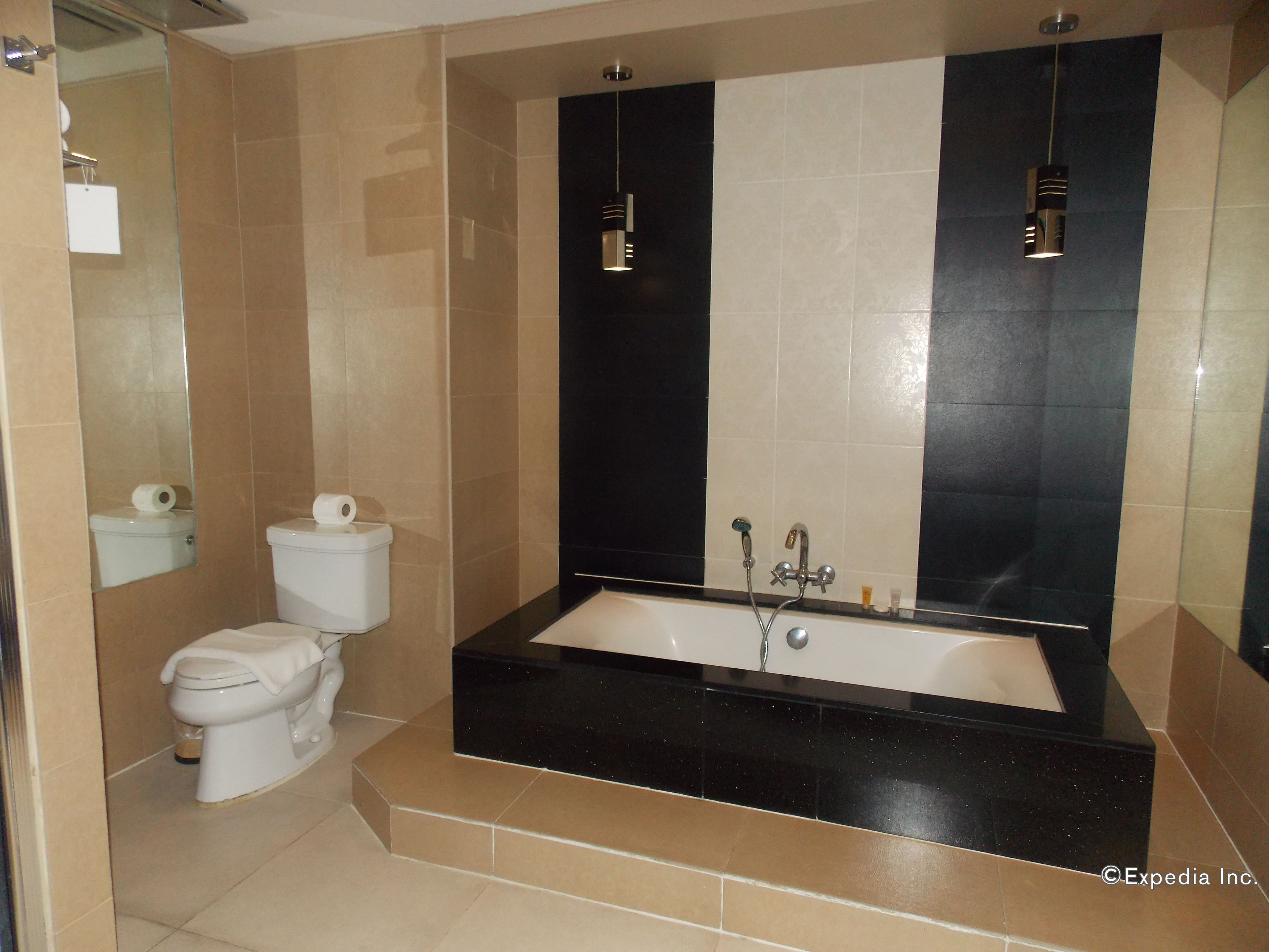 Un baño moderno con una bañera negra, un inodoro y un espejo grande.
