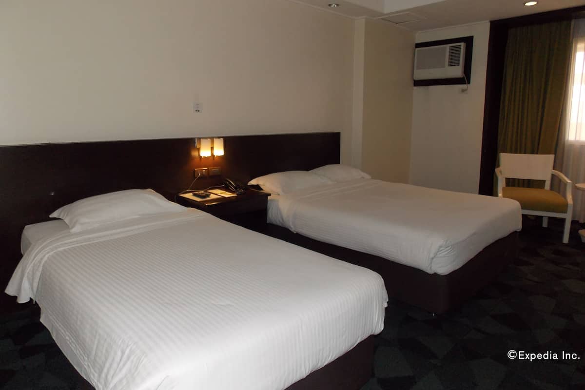 A hotel room with two single beds, a bedside table with a lamp, a chair, and a window with curtains.