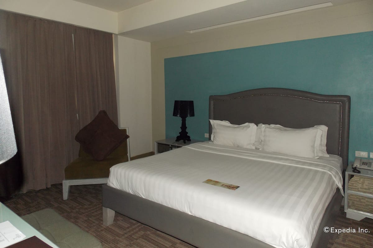 A hotel room with a large bed, a chair, a nightstand, and a lamp.