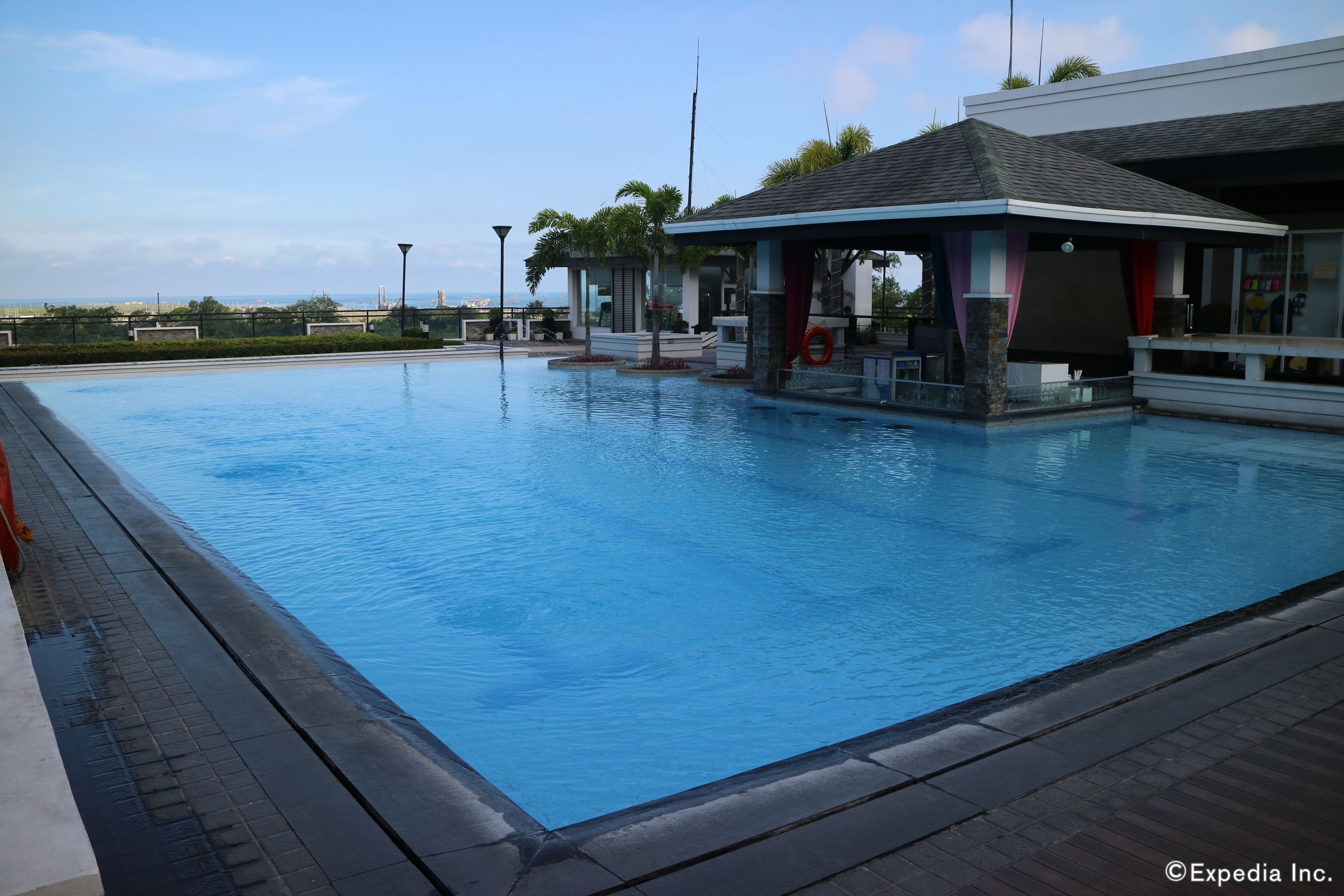 A swimming pool with a covered area, a view of the sea, and a modern building with a red accent.