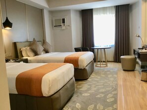 A hotel room with two beds, a desk, a chair, and a small table.