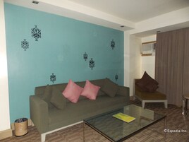 Una sala de estar con una pared color turquesa, una mesa de centro de vidrio, un sofá gris con cojines rosa y marrón, y un sillón marrón.