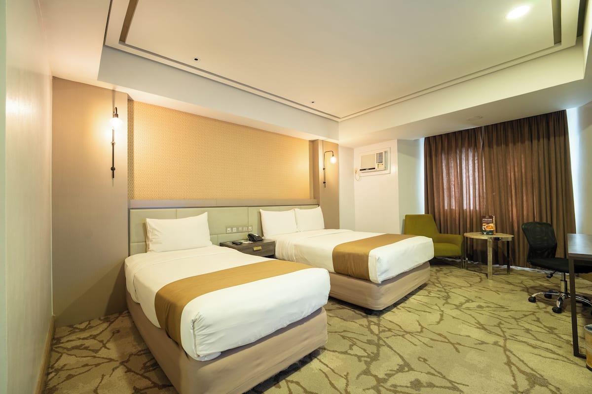 A hotel room with two beds, a desk, a chair, a small table, and a window with curtains.