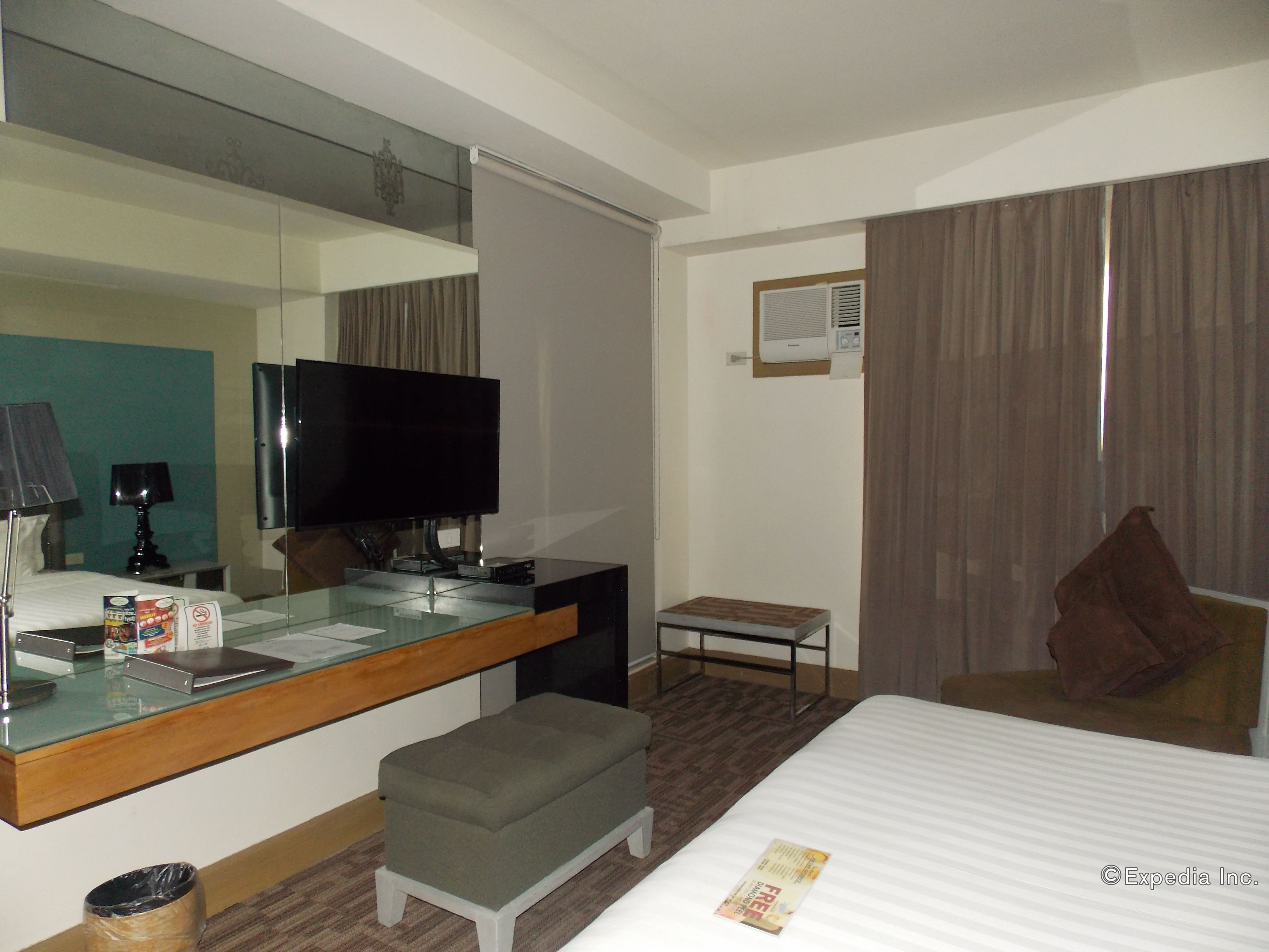 A hotel room with a bed, a TV, a desk with a computer, a small table, and a mirror.