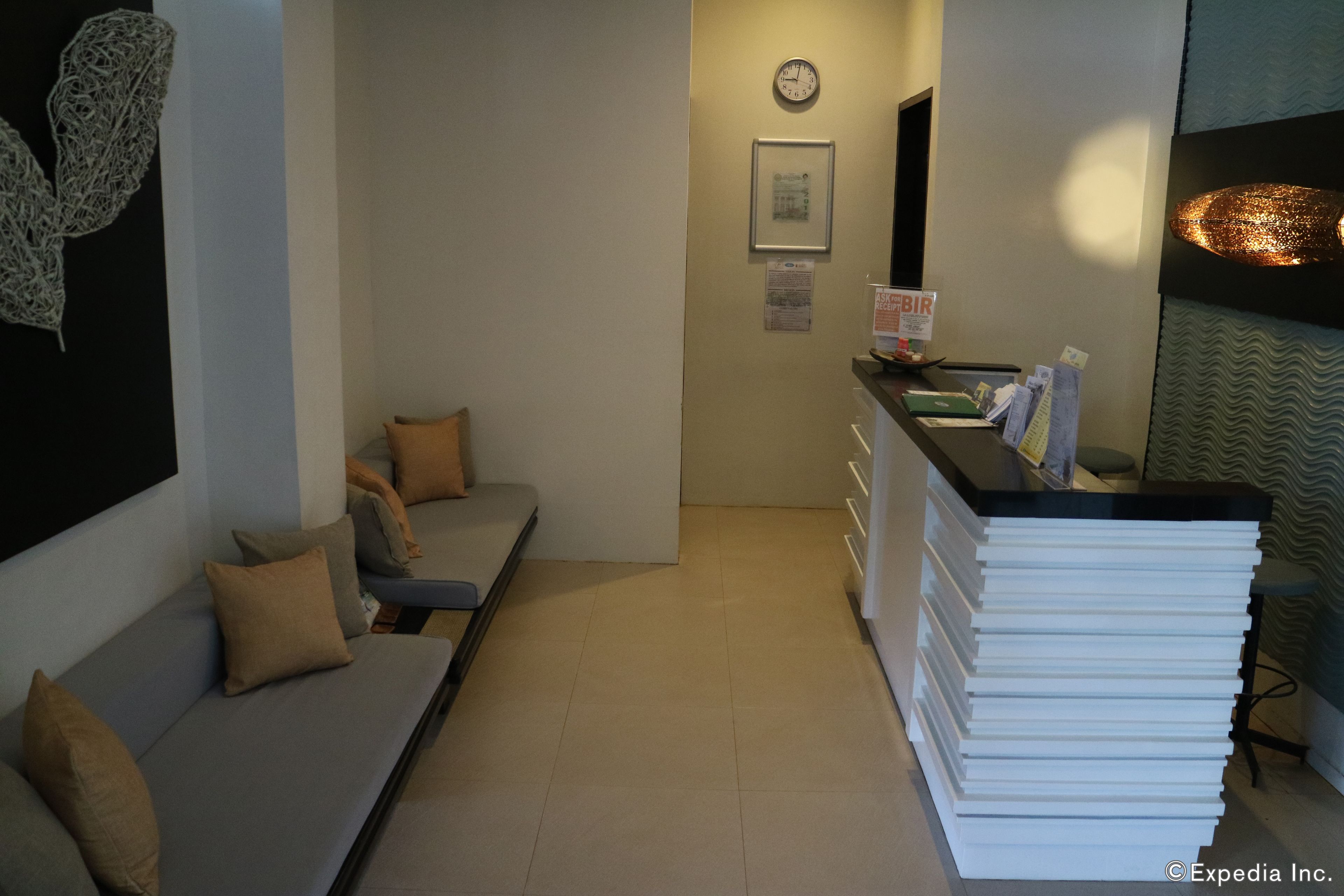 Zona de recepción de un hotel con un sofá, una pila de carpetas blancas, un reloj y un cuadro en la pared.