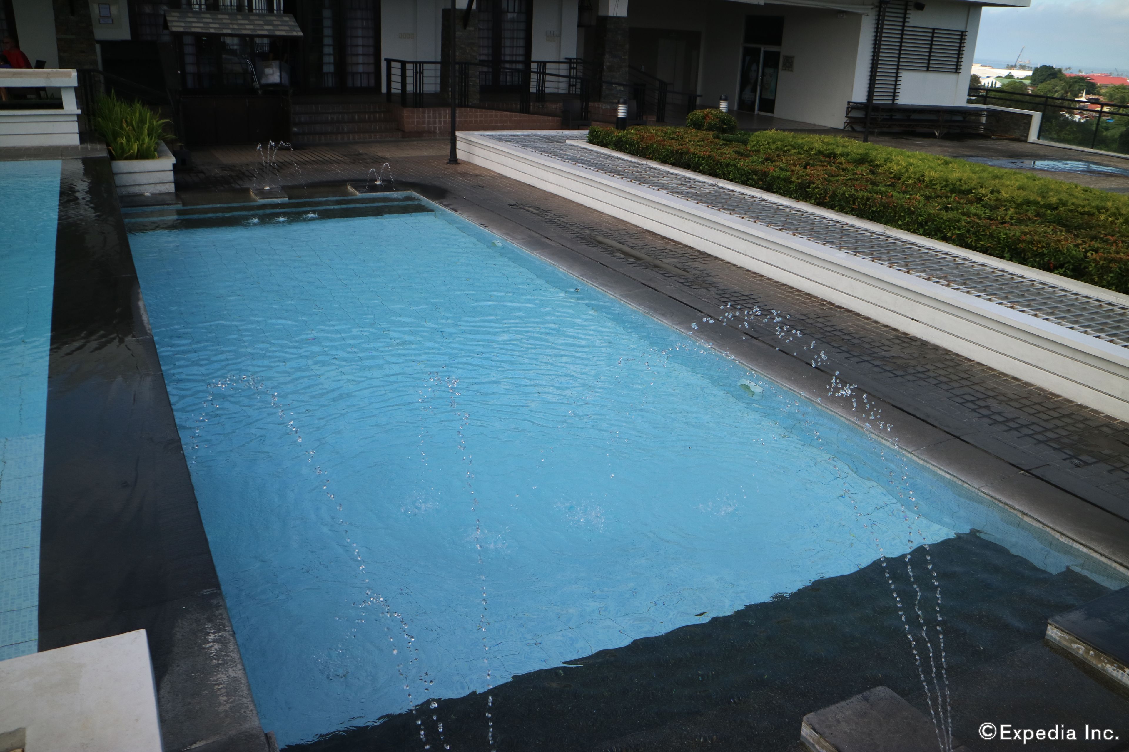 Une piscine rectangulaire à l’eau claire, entourée d’une allée pavée et d’une haie basse.