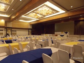 Un salón de conferencias con filas de mesas y sillas, un escenario y una pantalla grande.