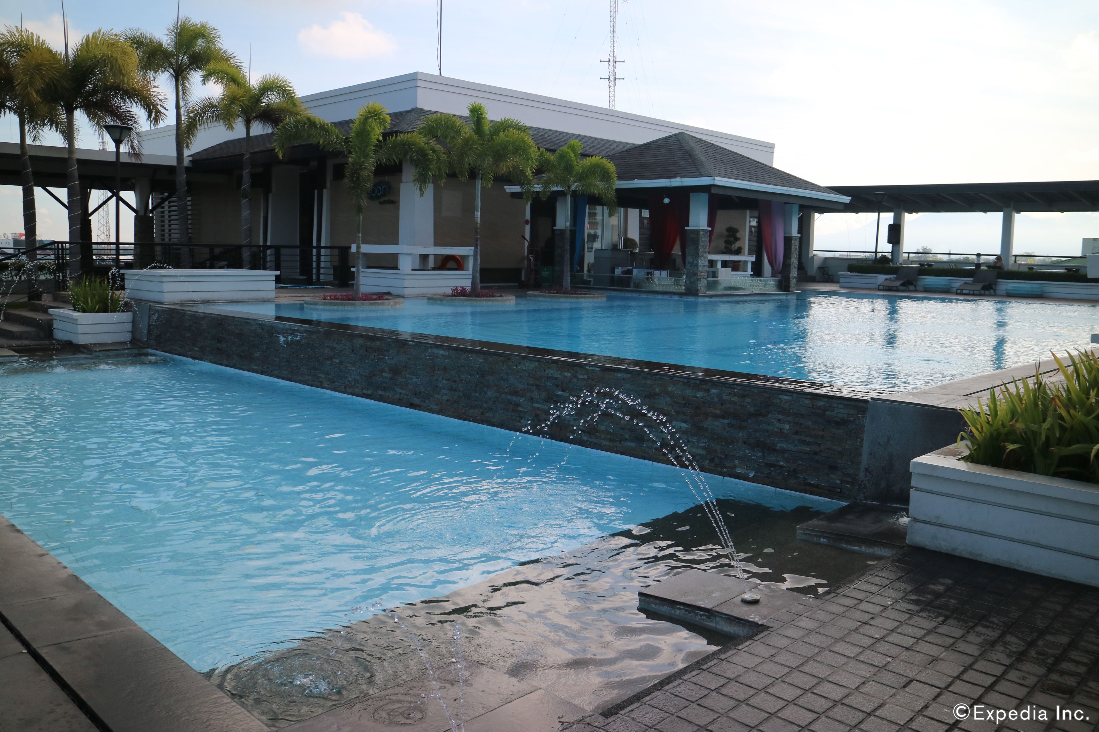 Una piscina con elemento d'acqua, circondata da palme e un edificio con patio coperto.
