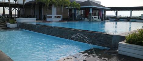 Una piscina con elemento d'acqua, circondata da palme e un edificio con patio coperto.