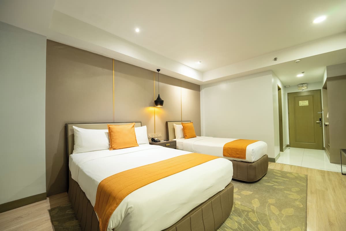 A hotel room with two beds, a nightstand, a lamp, and a door leading to another room.