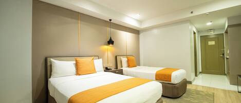 A hotel room with two beds, a nightstand, a lamp, and a door leading to another room.