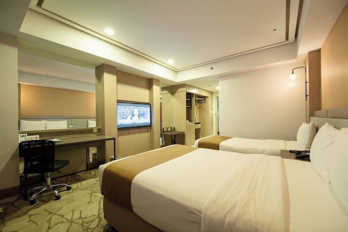 A hotel room with two beds, a desk, a chair, a television, and a mirror.