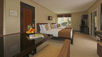 A hotel room with a bed, a desk with a fruit bowl, a magazine, and a television.