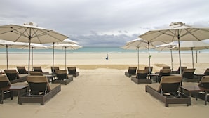 A beach with lounge chairs and umbrellas, a person walking on the sand, and the ocean in the background. - Two Seasons Boracay Resort (Boracay Island)