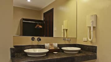 A bathroom with two sinks, a mirror, a towel rack, a trash can, and a phone.