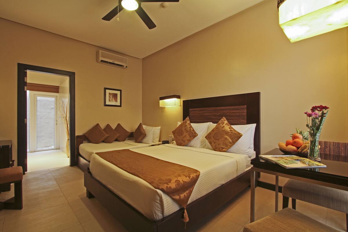Habitación de hotel con una cama grande, un escritorio con un jarrón de flores y un ventilador de techo.