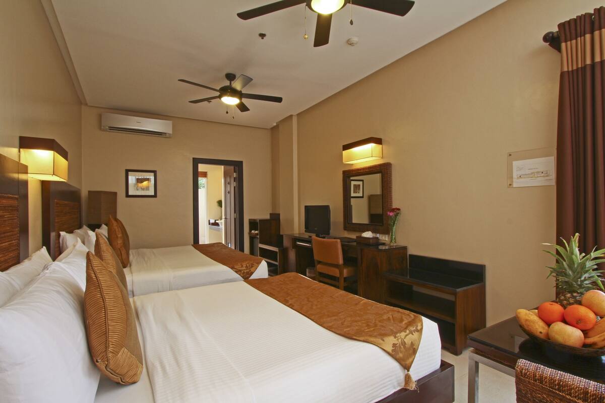 Habitación de hotel con dos camas, un escritorio, una silla, un televisor y un frutero.