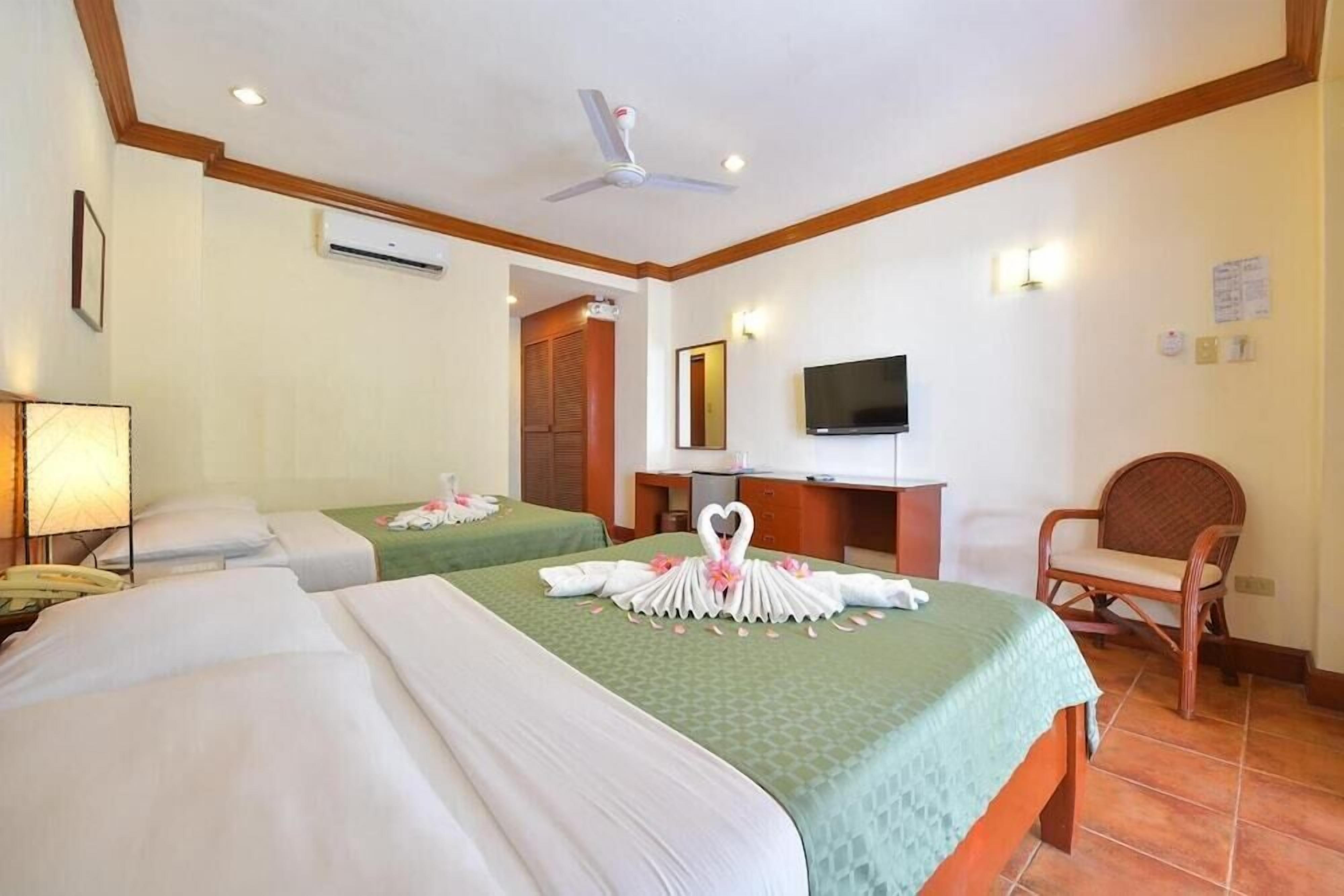 A hotel room with two beds, a desk with a flat-screen TV, a chair, and a ceiling fan.