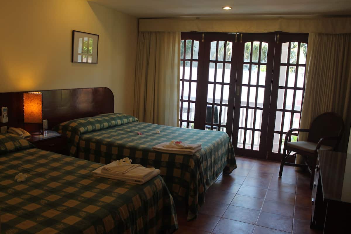 Une chambre d’hôtel avec deux lits, un bureau, une chaise et une fenêtre avec des rideaux.