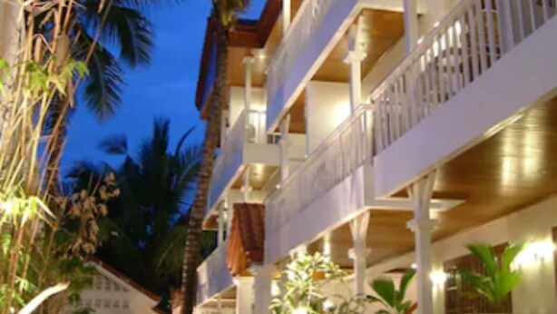 Un hotel de varios pisos con balcones, mobiliario exterior y palmeras.