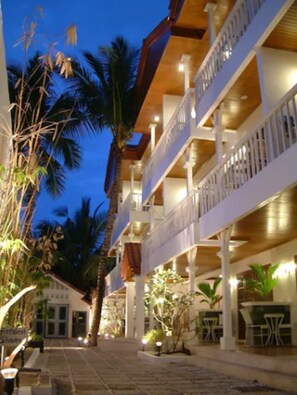 A multi-story hotel with balconies, outdoor seating, and palm trees.