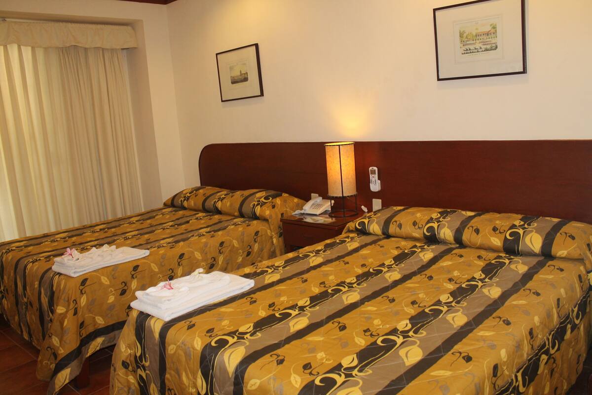 Une chambre d’hôtel avec deux lits, une table de chevet avec une lampe et un téléphone.