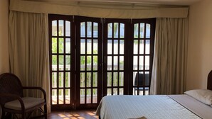 Una habitación de hotel con cama, una silla y un ventanal con cortinas.