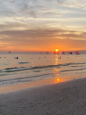 A beach at sunset with sailboats and people in the water. - Nigi Nigi Nu Noos “e” Nu Nu Noos (Boracay Island)