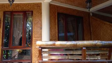 A wooden bench outside a building with a textured wall and two windows with curtains.