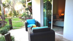 Un espace extérieur moderne aménagé avec un canapé en osier et une table, entouré d’un jardin bien entretenu où poussent différentes espèces de plantes, et agrémenté d’un chemin en pierre.