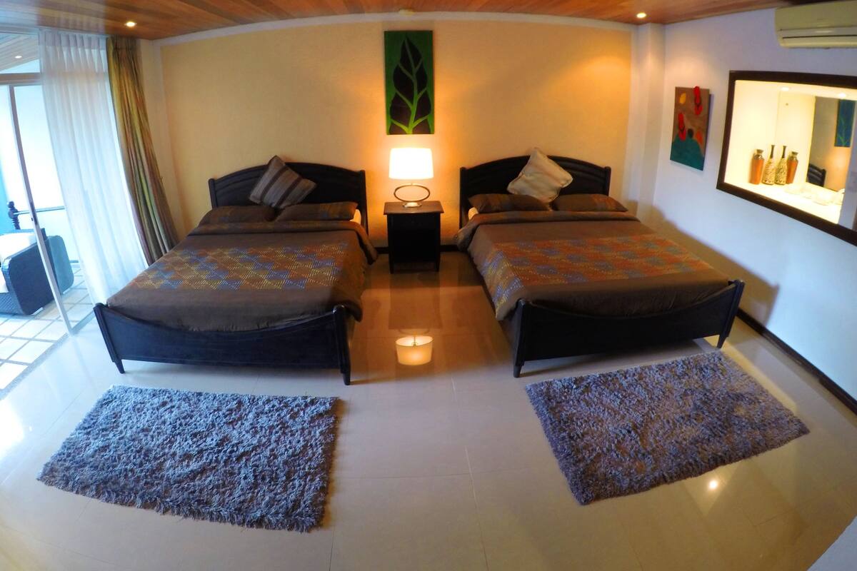 Una habitación de hotel moderna con dos camas, una mesita de noche, una lámpara y un ventanal con cortinas.