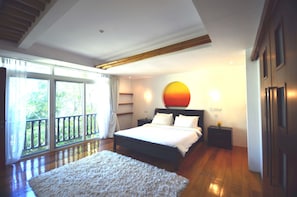 A bedroom with a large bed, a nightstand, a wall-mounted lamp, and a view through a sliding door to an outdoor balcony.