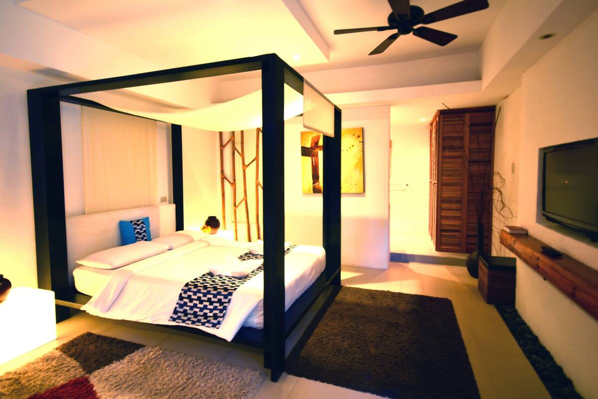 Una cama con dosel en una habitación con ventilador de techo, televisión y un mueble de madera.