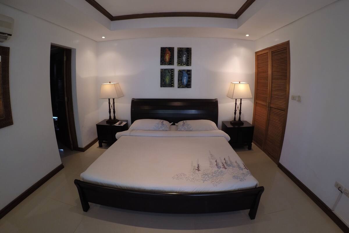 Un dormitorio con una cama grande, dos mesitas de noche con lámparas, una lámpara de techo y una obra de arte en la pared.
