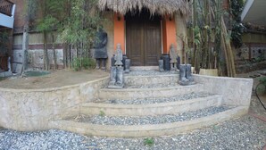 Un bâtiment traditionnel avec un toit de chaume, des marches en pierre menant à une porte en bois et des statues de personnages.
