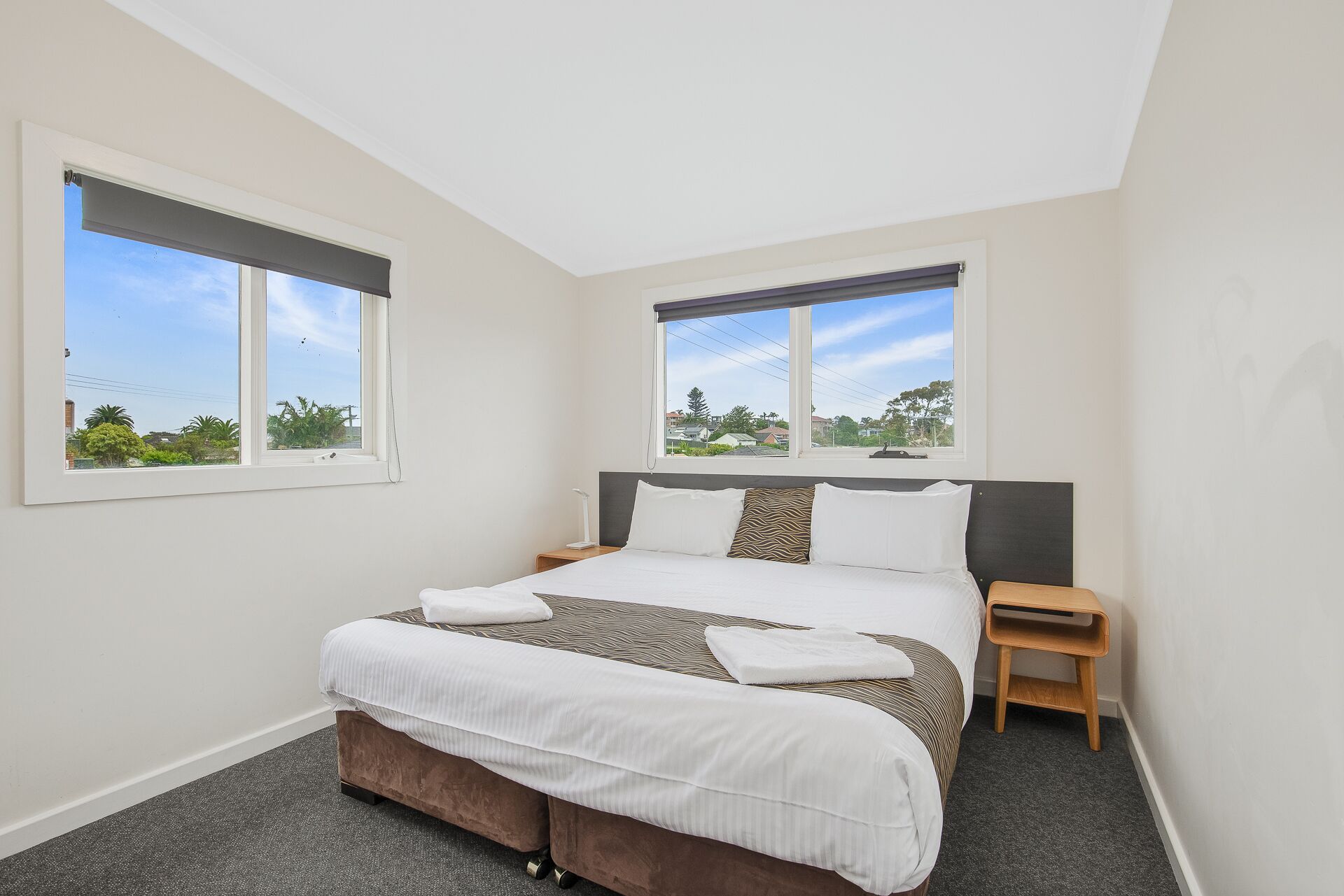 A bedroom with a bed, two bedside tables, and two windows.